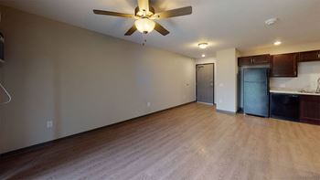 an empty living room with a ceiling fan and a kitchen in the background